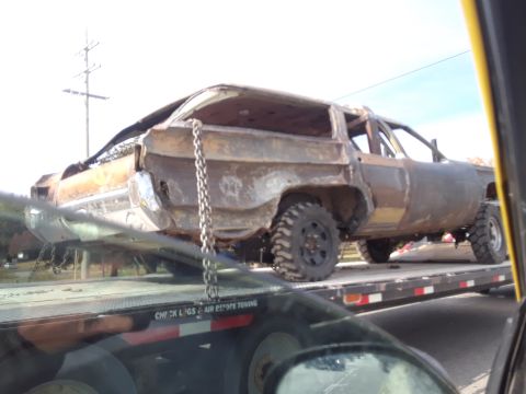 1994 Ford Bronco - A heavily modified and rusted station wagon is being transported on a flatbed tow truck.
