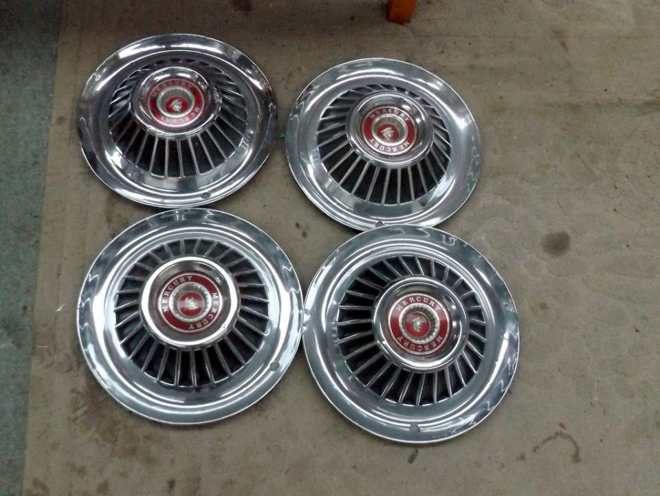 Four chrome hubcaps with red Mercury emblems. Likely from a 1964 model