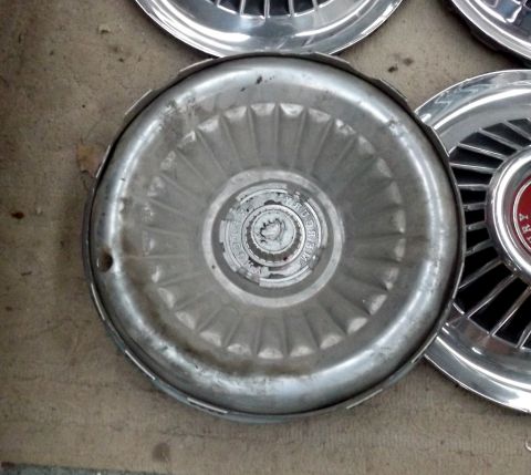 1964 Mercury Monterey - Several used hubcaps are laid out on a concrete surface, with one clearly displaying a Mercury emblem.