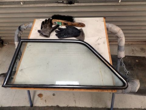 1962 MG B - Car door window assembly with chrome trim, gloves, and brush on a workbench.
