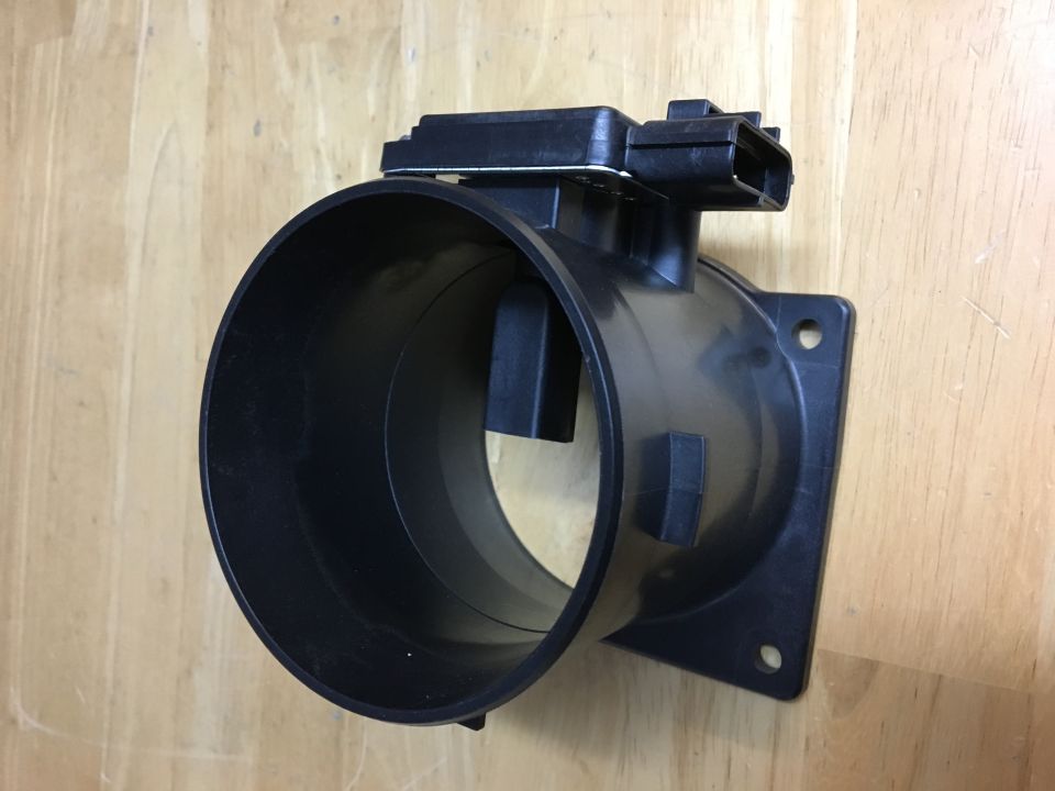 Black plastic mass air flow sensor with electrical connector, resting on a wooden surface