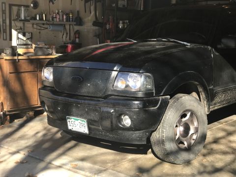 2000 Ford Explorer - A black Ford Ranger pickup truck is parked in a garage, showing its front grille and headlights.