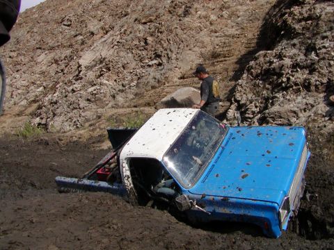 2000 Ford F-450 - A blue and white square-body pickup buried to the frame in deep mud at the base of a rocky hill, mud spattered across the hood and roof and…
