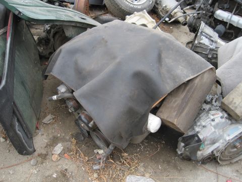 1989 Ford Bronco - Scrap yard scene with engine components and a tarp-covered item.
