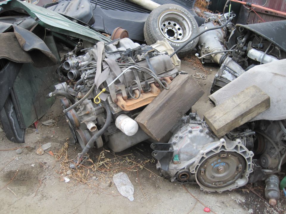 Engine and transmission components piled in a junkyard with a tire visible