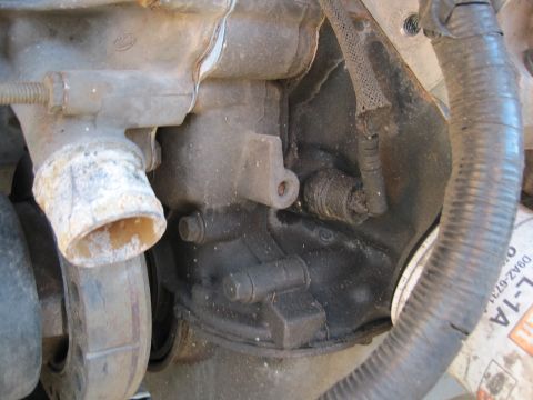 1989 Ford Bronco - Close-up of an engine block with various components attached, including hoses and a pipe.