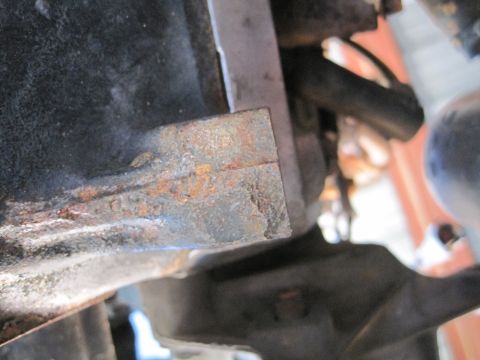 1989 Ford Bronco - A close-up view of a rusty metal bracket attached to a dark component, likely part of an engine.