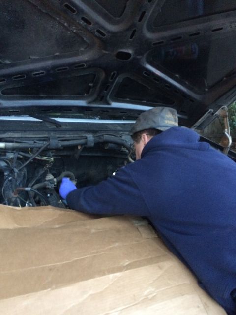 1989 Ford Bronco - A person works on the engine of a vehicle with the hood up.