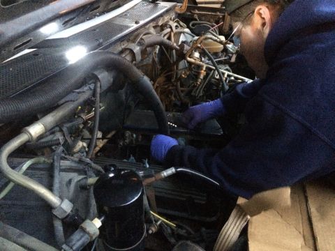 1989 Ford Bronco - A person is performing maintenance on a vehicle's engine compartment, surrounded by various engine components and hoses.