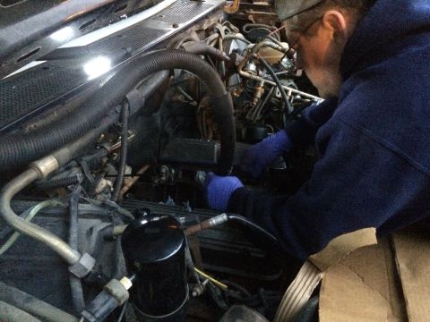1989 Ford Bronco - Mechanic works on an engine bay, surrounded by hoses and electrical components.