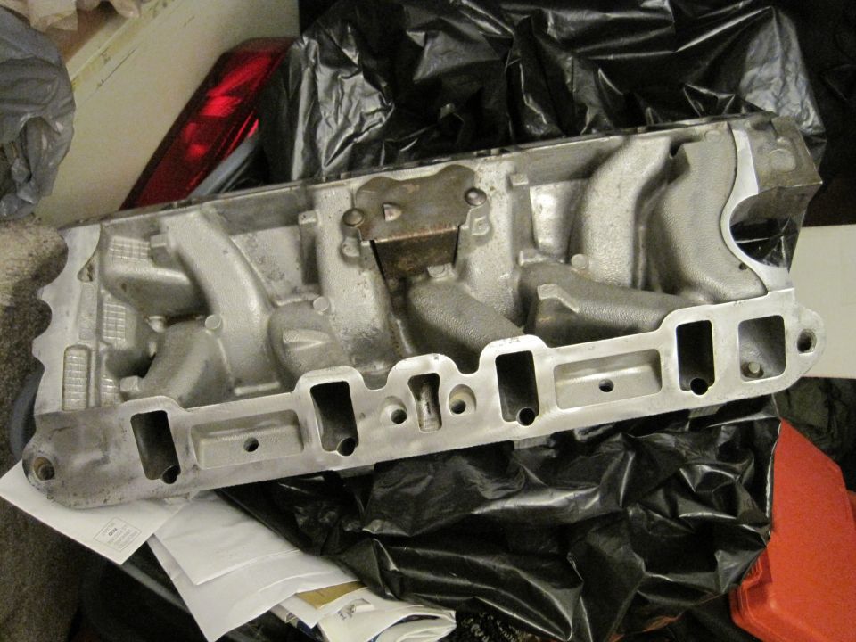 Aluminum engine intake manifold with multiple runners, resting on black plastic sheeting