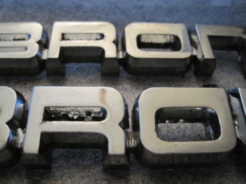 1989 Ford Bronco - Chrome Bronco emblems are shown up close, revealing some damage and wear.