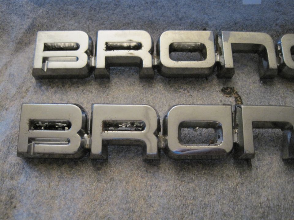 Two chrome Bronco emblems, one above the other, on a textured surface