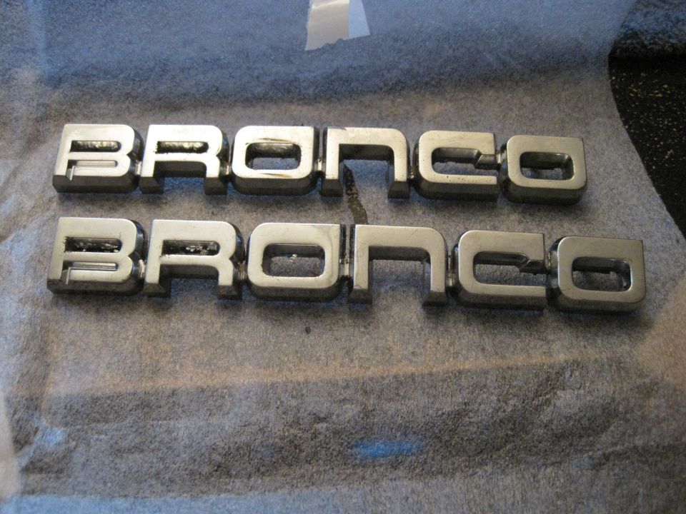 Two sets of chrome Bronco emblems laid out on a gray surface
