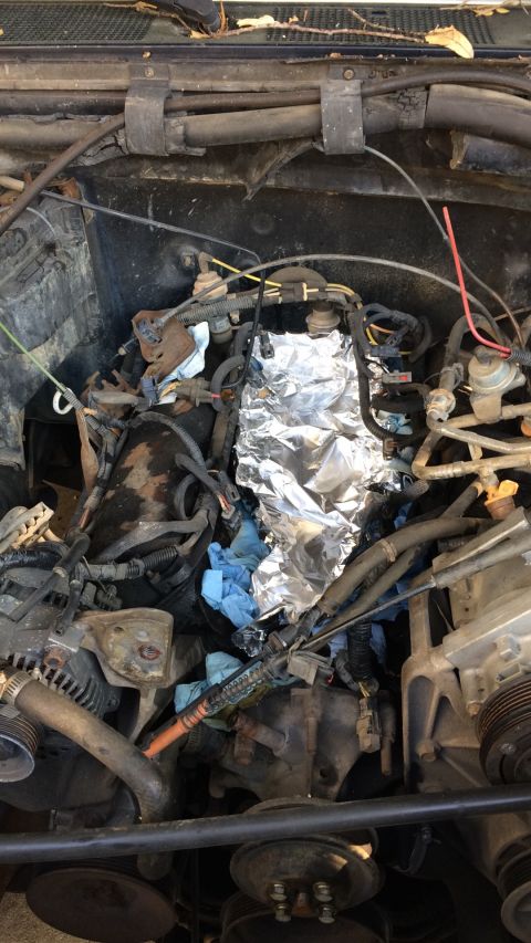 1989 Ford Bronco - The engine bay of a vehicle is shown with parts covered in aluminum foil and blue shop towels.