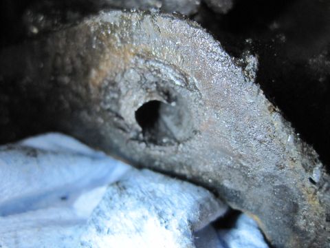 1989 Ford Bronco - A close-up view of a damaged and corroded metal component, possibly from an engine, with a visible hole.