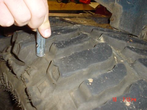 1983 Ford Bronco - A gauge is used to measure the tread depth of a large off-road tire, indicating wear or remaining life.
