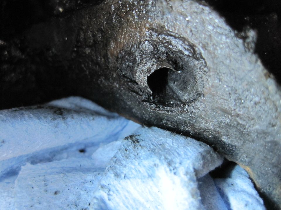 Close-up of a dark, oily engine component with a hole, resting on blue shop towels