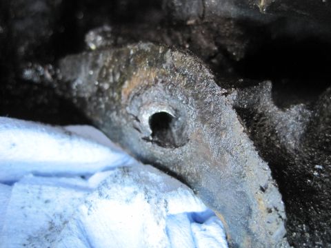 1989 Ford Bronco - A close-up view of a dirty engine part, possibly a bracket or mounting piece, with a circular opening.