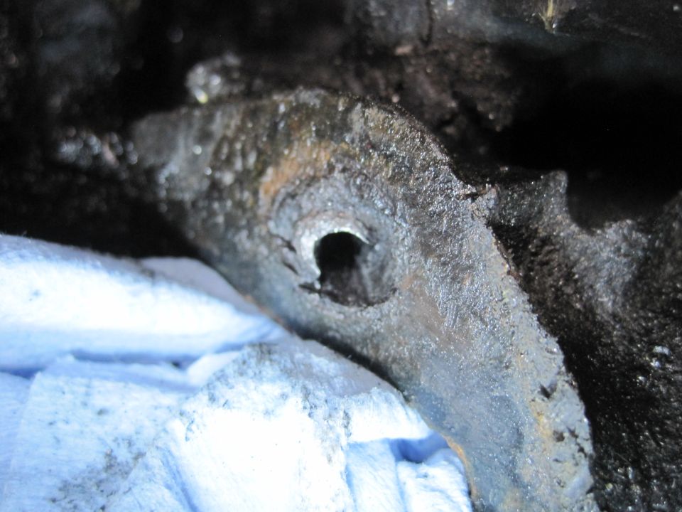 Close-up of a greasy, corroded metal engine component with a hole