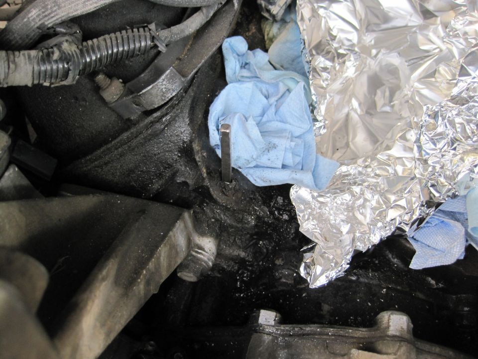 Engine oil dipstick partially inserted into its tube, with blue shop towels and aluminum foil nearby