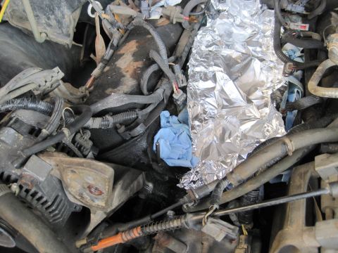 1989 Ford Bronco - Close-up view of a vehicle's engine compartment, showing various components and a section wrapped in aluminum foil.