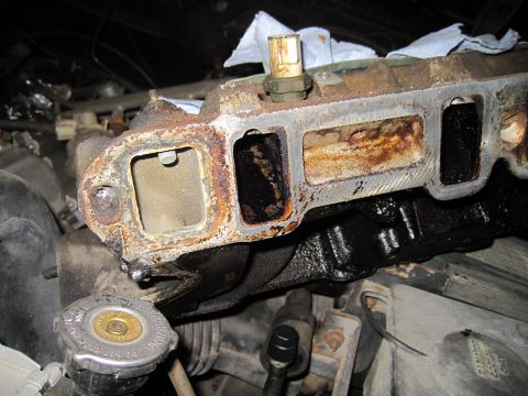 1989 Ford Bronco - This is a close-up view of a heavily corroded engine intake manifold, likely in need of replacement or cleaning.