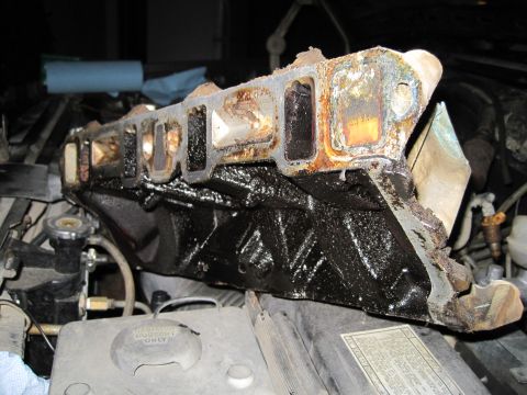 1989 Ford Bronco - Engine intake manifold covered in black sludge and rust, seen during reassembly.