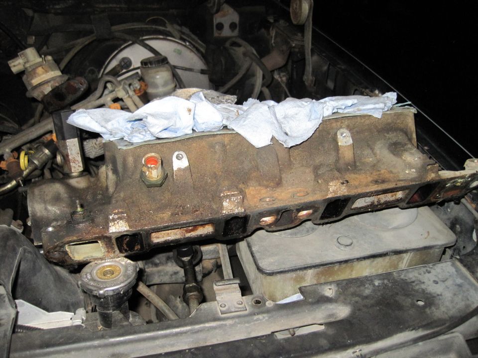 Engine intake manifold removed from vehicle, resting on engine components. White paper towels cover part of the manifold