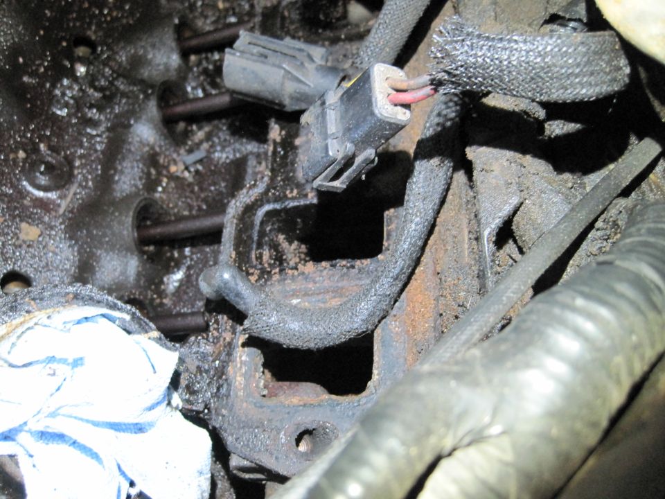 Close-up of engine block with bolts and a wiring harness connector. Some white cloth is visible
