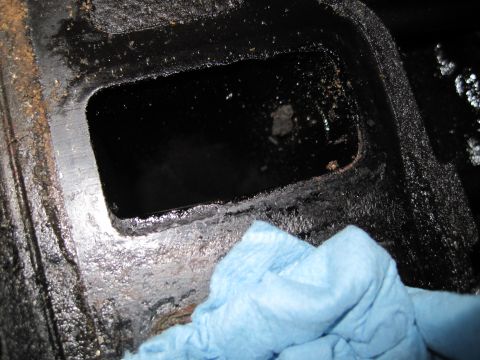1989 Ford Bronco - A blue shop towel is used to wipe down an opening in a dirty, oil-covered engine block.
