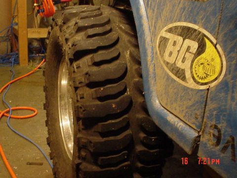 1983 Ford Bronco - A close-up view of a large, aggressive off-road tire and a portion of a blue vehicle's fender with a logo.