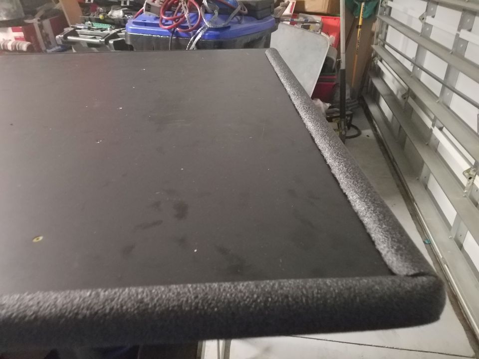 Black surface with foam edge trim, seen from above at an angle. A garage door is visible in the background
