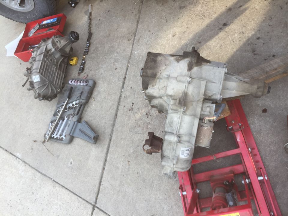 Two transfer cases, one on a red jack, with a toolbox and wrenches on concrete