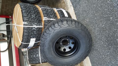 1994 Ford Bronco - Four new off-road tires and black rims are stacked and ready for installation.