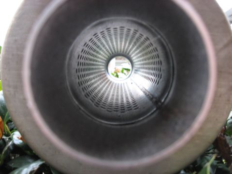 1987 Jaguar XJ6 - Interior view of a perforated exhaust pipe, showing the baffle and a glimpse of greenery beyond.