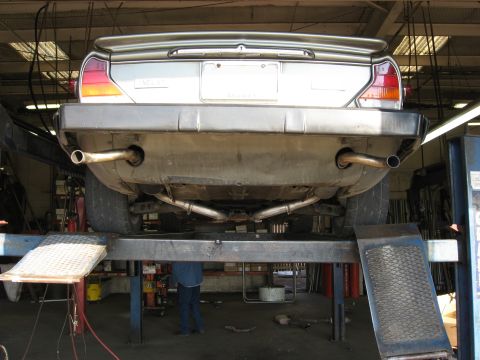 1987 Jaguar XJ6 - The rear of a 1987 Jaguar XJ6 is shown on a lift, focusing on its dual exhaust system.