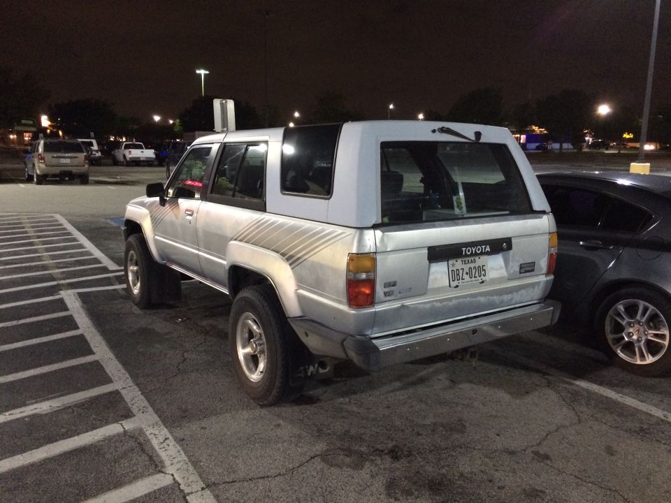 Silver Toyota 4Runner parked at night. Has a light blue camper shell