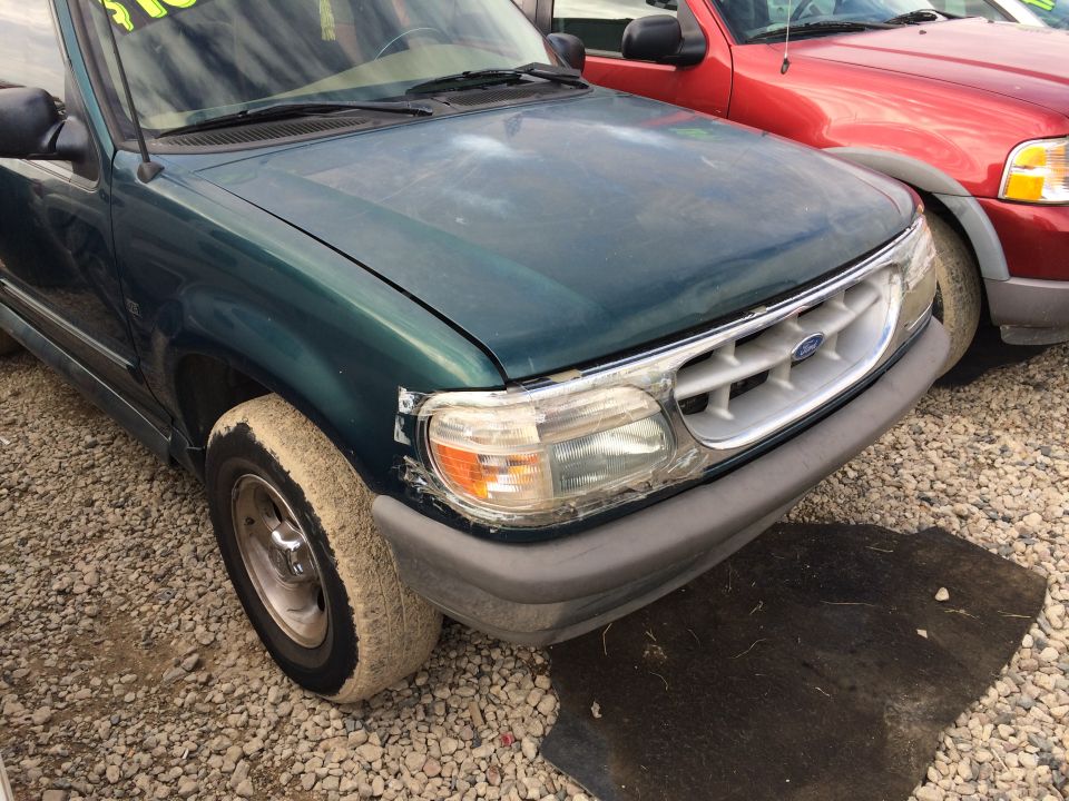Green Ford Explorer front end with damaged headlight and chrome grille. Red SUV behind it