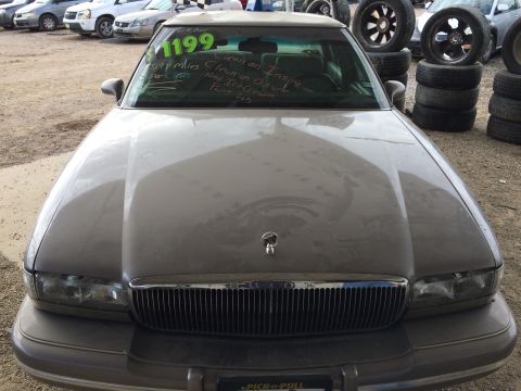 1985 Jaguar XJ6 - A dusty sedan sits in a junkyard, with handwritten notes on the windshield indicating price and condition.