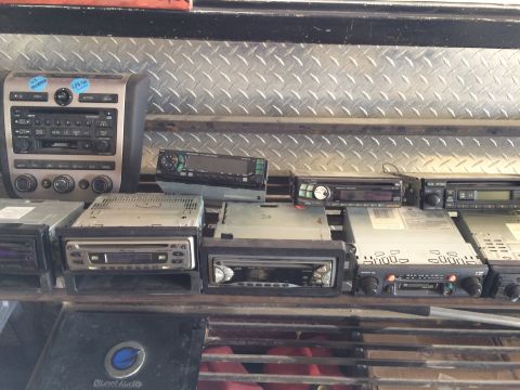 1985 Jaguar XJ6 - A collection of various car stereos are displayed on metal shelves, some with visible brand names and model numbers.