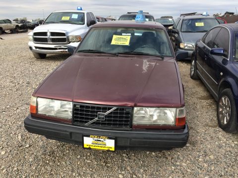 1985 Jaguar XJ6 - A maroon Volvo sedan sits in a junkyard with other vehicles around it.