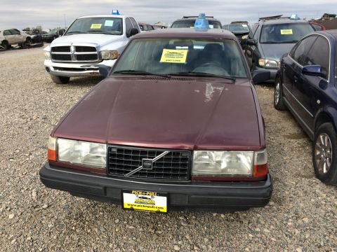 1985 Jaguar XJ6 - A maroon Volvo sedan is parked in a junkyard with other vehicles visible in the background.