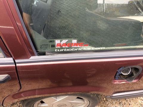 1985 Jaguar XJ6 - A maroon Volvo sedan is seen from the side, with a racing sticker on the window and an open fuel door.