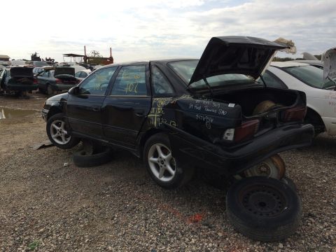 1985 Jaguar XJ6 - A black sedan sits in a junkyard with its trunk open and wheels removed.