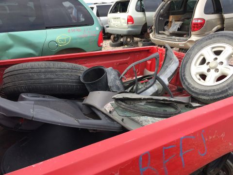 1985 Jaguar XJ6 - A collection of assorted car parts are piled in the bed of a red pickup truck at a junkyard.
