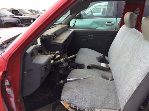 1985 Jaguar XJ6 - Interior view of a red car with worn seats and visible wiring, parked in a junkyard.