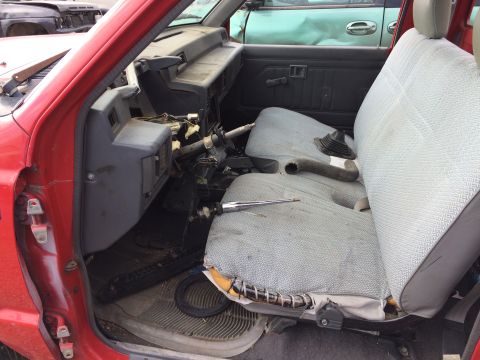 1985 Jaguar XJ6 - The interior of a red pickup truck is visible, with worn seats and a damaged dashboard, suggesting it is a junkyard vehicle.