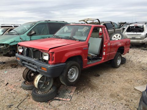 1985 Jaguar XJ6 - Junkyard scene with a red pickup truck missing parts, next to a green minivan and other vehicles.