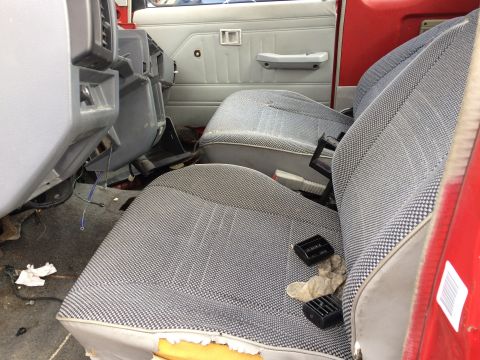 1985 Jaguar XJ6 - The interior of a red vehicle shows worn seats and disarray, with visible wires and broken dashboard parts.